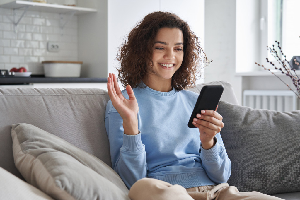 A modern woman smiling while she uses her phone on her cozy couch