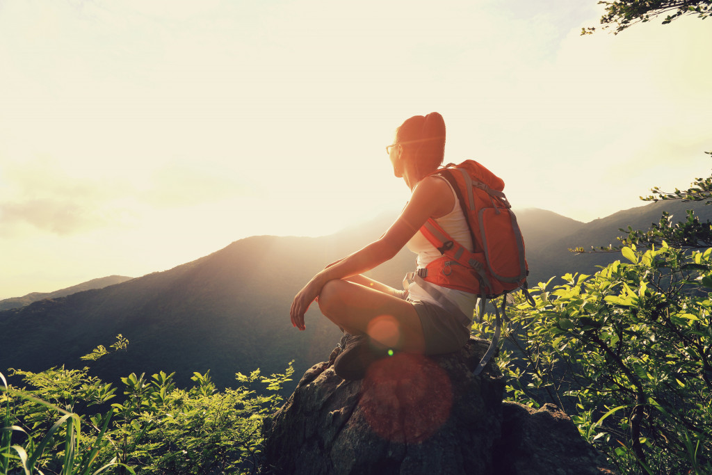 female adventurer sitting on top a rock alongside a cliff with her backpack