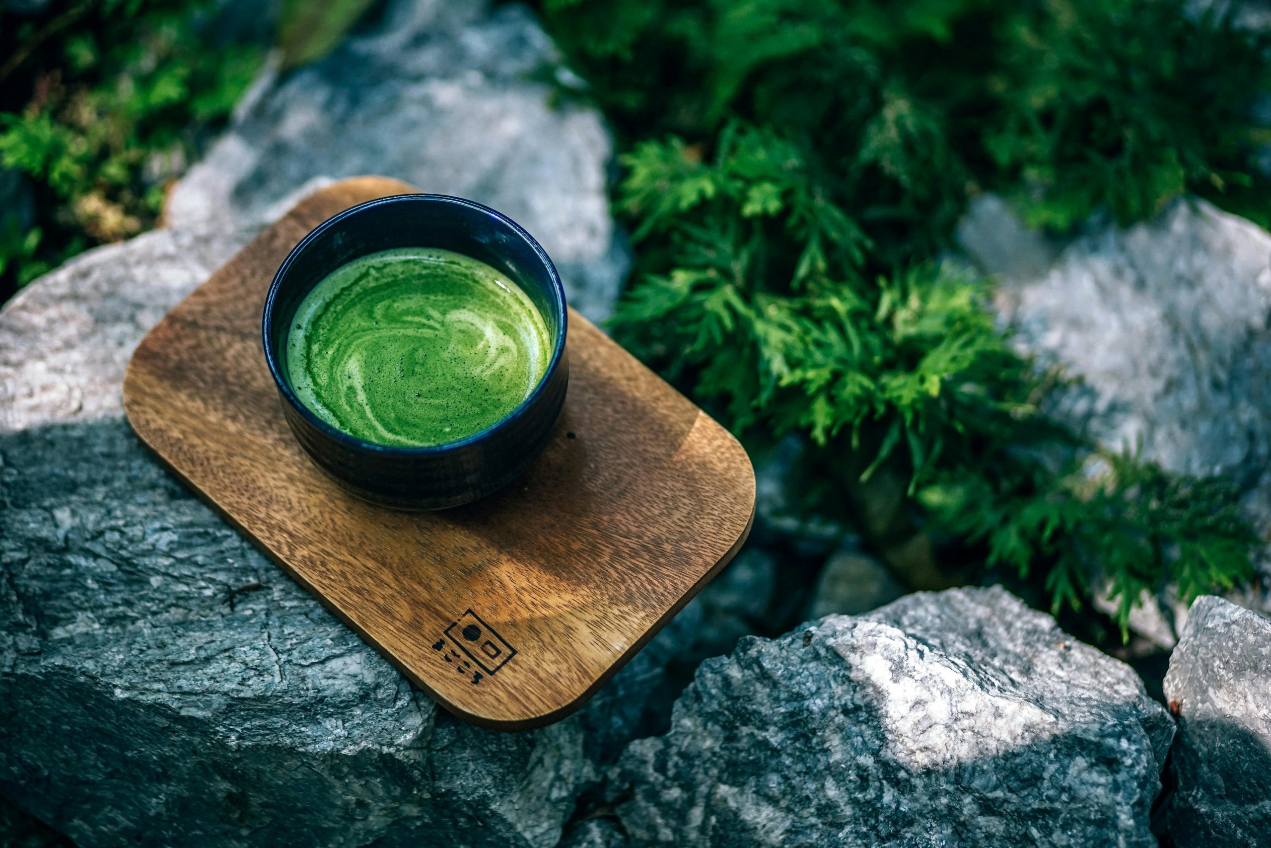 cup of matcha on a wooden tray, displayed in a zen garden