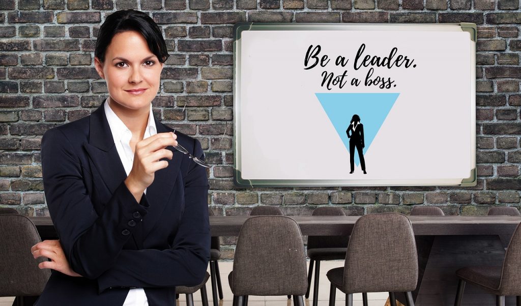 Professional woman standing confidently in an office with a whiteboard that says ‘Be a leader, not a boss’