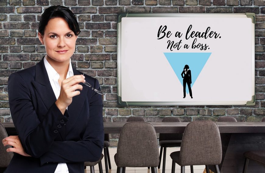 Professional woman standing confidently in an office with a whiteboard that says ‘Be a leader, not a boss’