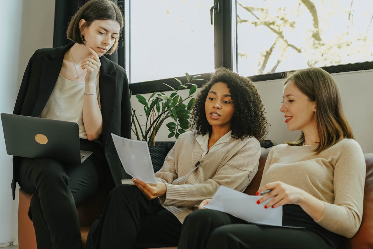 Three professional women discussing documents and demonstrating confident, assertive communication during a meeting
